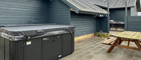 A covered outdoor area with a hot tub, picnic table, and chairs.
