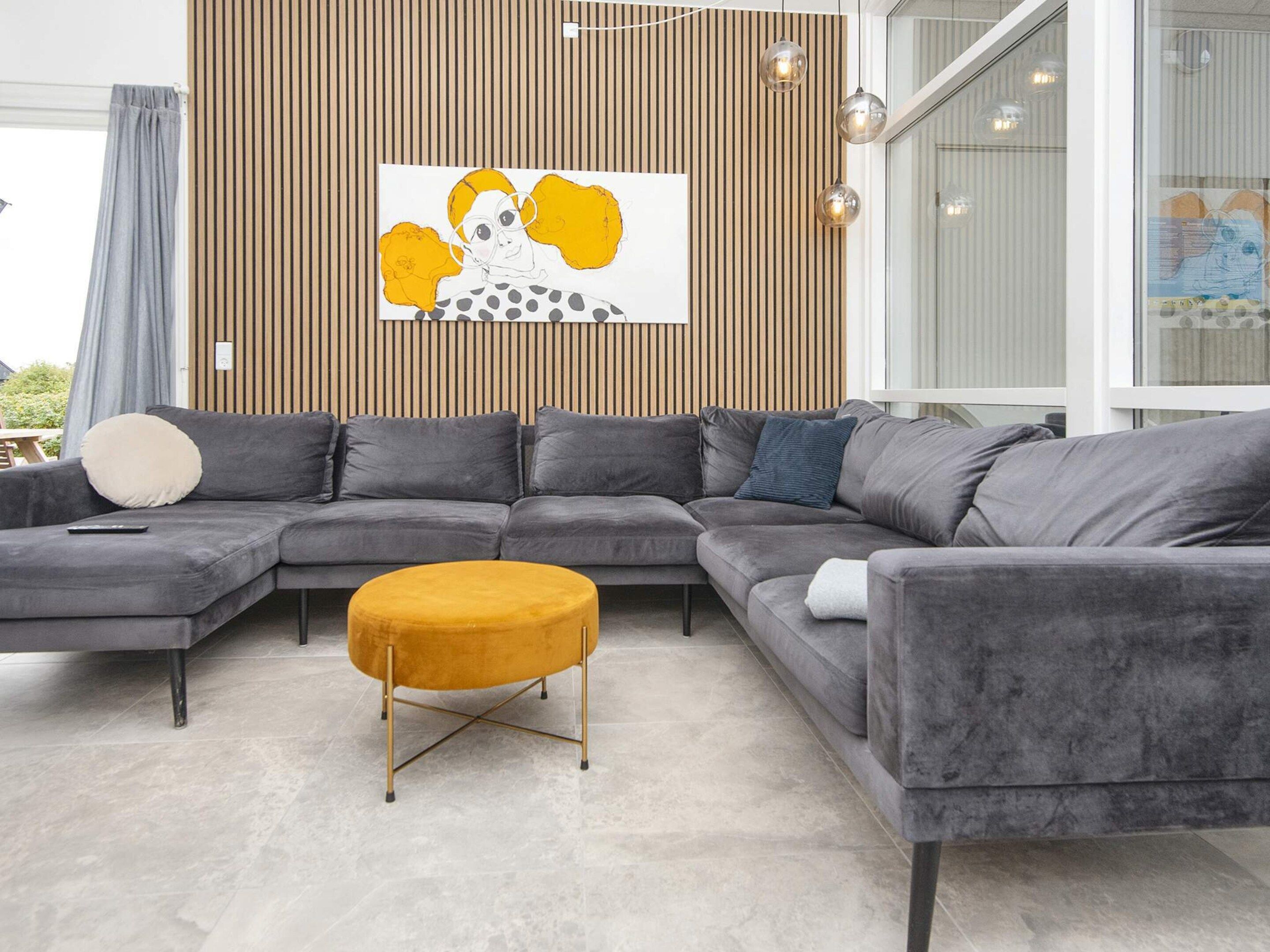 A modern living room with a sectional sofa, a round ottoman, and a wooden slatted wall with a framed artwork.