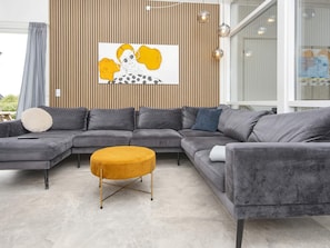A modern living room with a sectional sofa, a round ottoman, and a wooden slatted wall with a framed artwork. - 4 Star Holiday Home in Harboore (Harboore)
