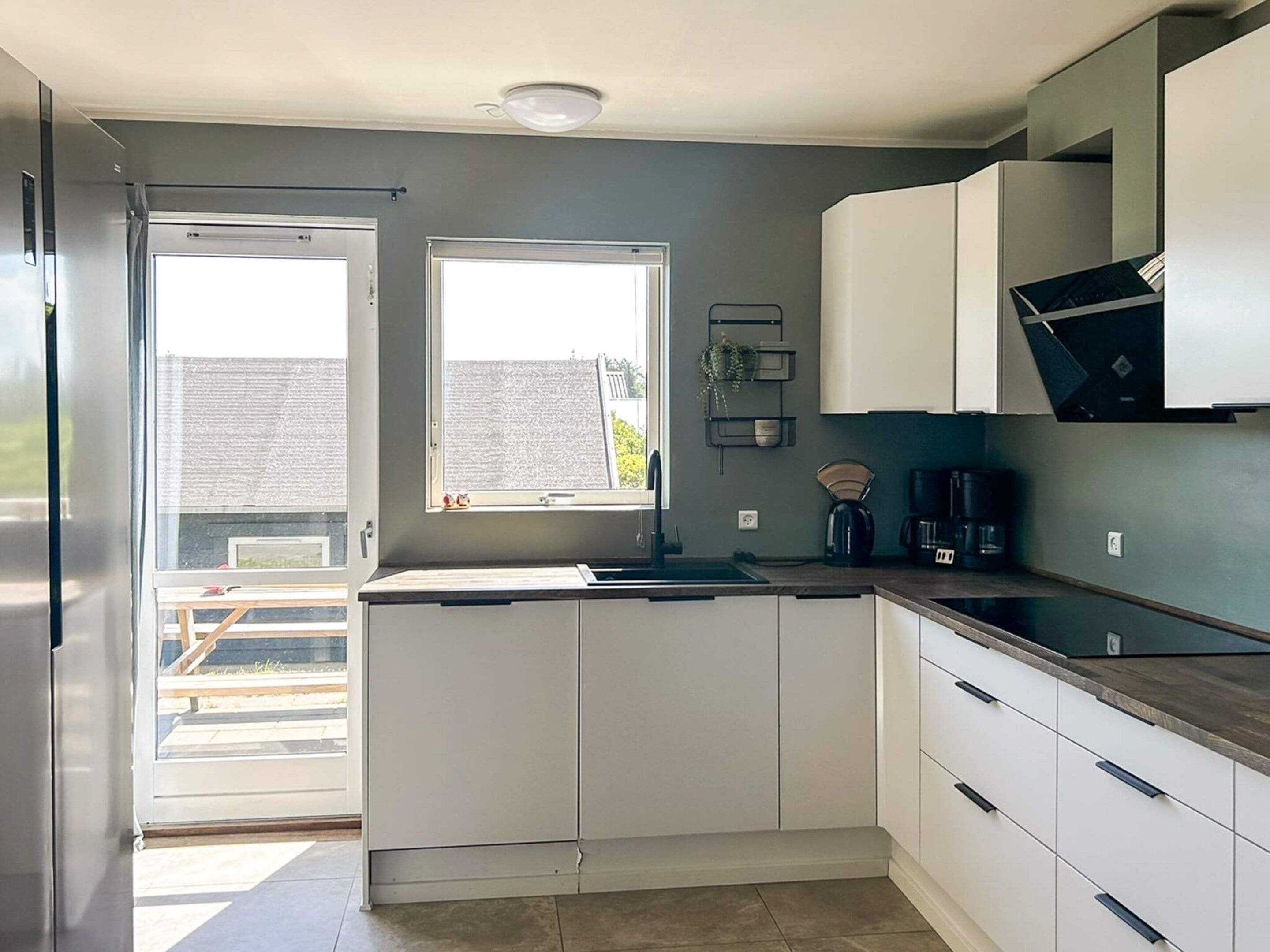Cozinha moderna com armários brancos, forno embutido e janela que proporciona iluminação natural.