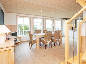 A dining area with a wooden table and wicker chairs, a kitchen in the background, and a staircase leading to another level.