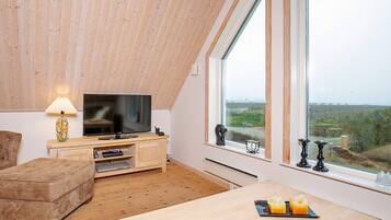 Uma sala de estar moderna com televisão, mobiliário de madeira e uma grande janela com vista para o campo.