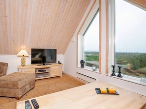 A modern living room with a television, wooden furniture, and a large window offering a view of the countryside.