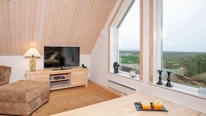 En moderne stue med tv, træmøbler og et stort vindue med udsigt over landskabet.