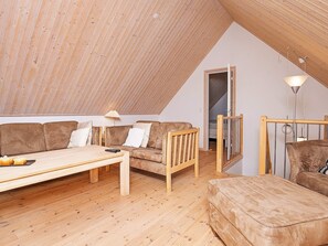 A loft-style room with a sloped ceiling, wooden flooring, a sofa set, a table, and a lamp. - 5 Star Holiday Home in Laeso (Læsø)