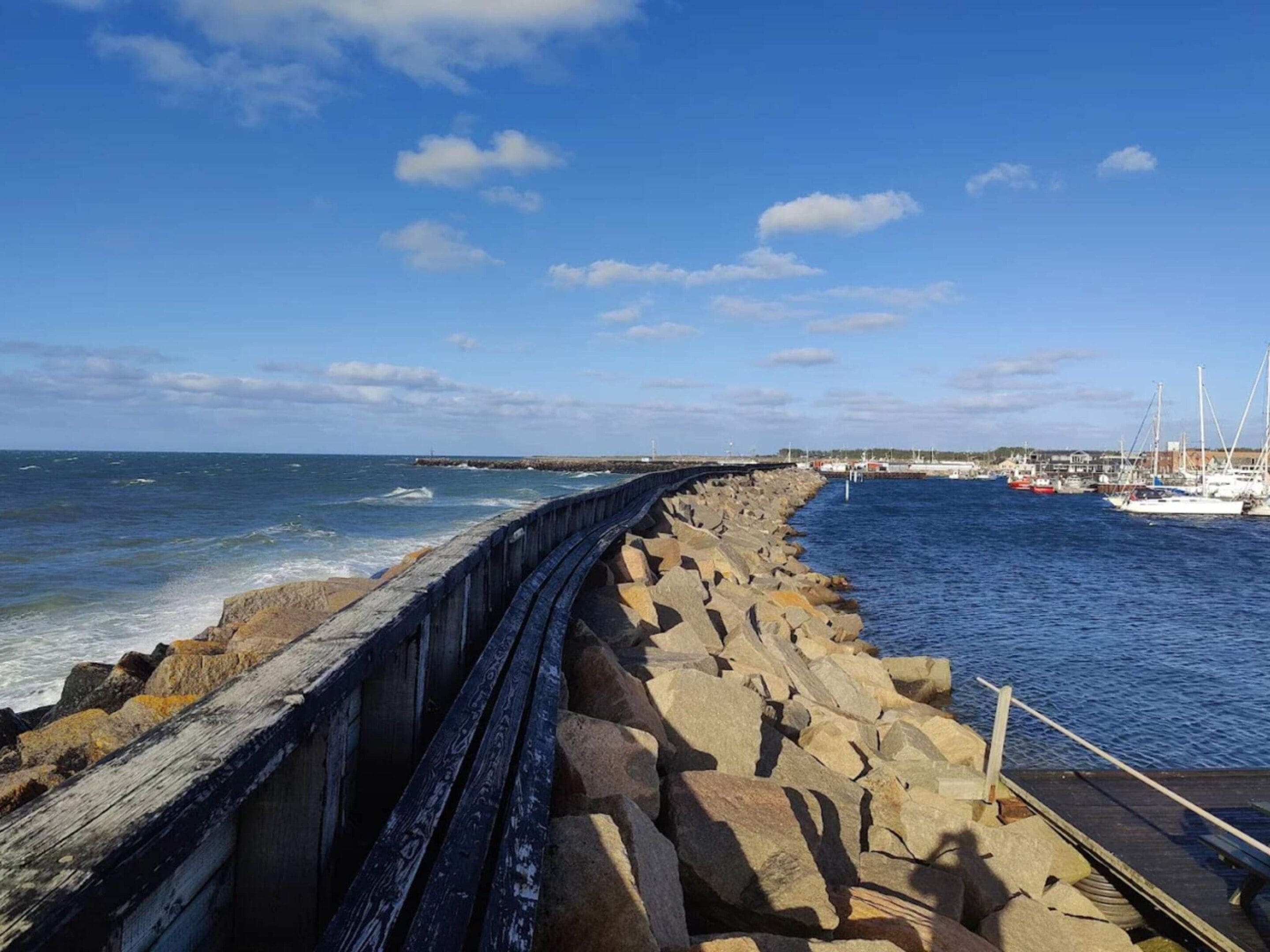 A rocky breakwater with boats docked in the background.