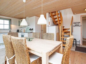 Una cocina moderna con armarios blancos, una escalera de madera y un comedor con sillas de mimbre y una mesa de madera.