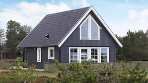 Et mørkt hus med saddeltag, vinduer med hvide rammer og en synlig skorsten.