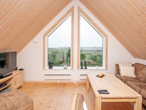 Quarto de sótão acolhedor com uma grande janela, piso de madeira, televisão, mesa e sofá.