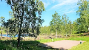 A paved area with a grassy border, surrounded by trees and a body of water in the background. - 4 Person Holiday Home in Axvall (Axvall)