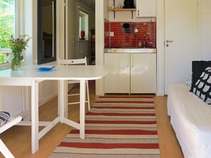 A compact living space with a kitchenette, a dining area with a table and chairs, a bed with a patterned pillow, and a striped rug. - 4 Person Holiday Home in Axvall (Axvall)