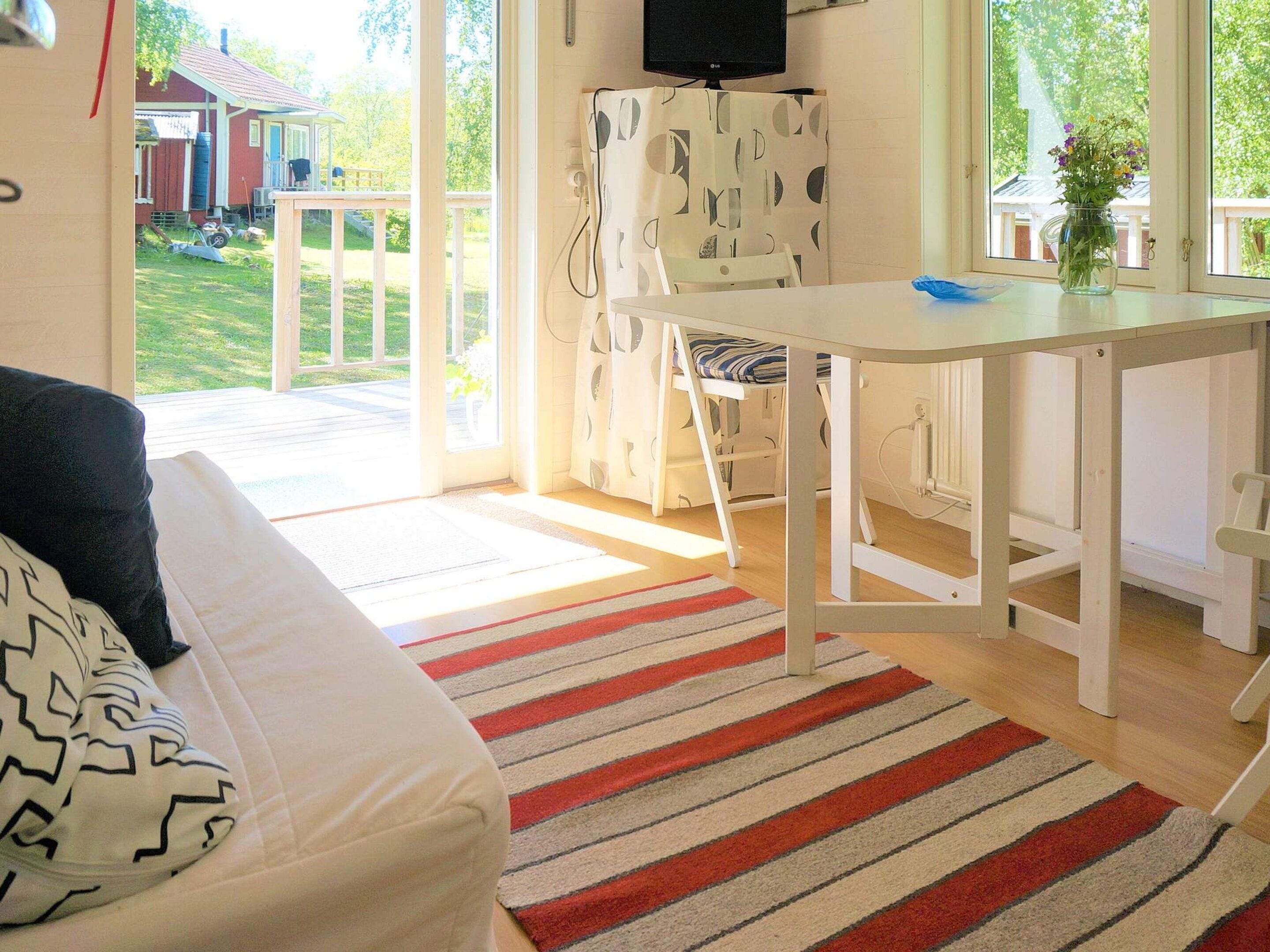 A room with a bed, a desk, a chair, a TV, and a window with a view of a house and greenery.