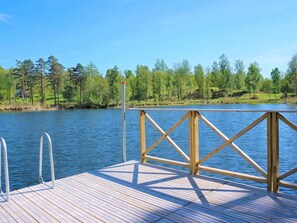 Une jetée en bois s’étendant au-dessus d’un lac paisible, entourée d’arbres et sous un ciel dégagé.