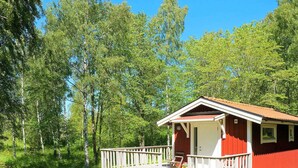 A red cabin with a porch and wooden deck, surrounded by trees. - 4 Person Holiday Home in Axvall (Axvall)