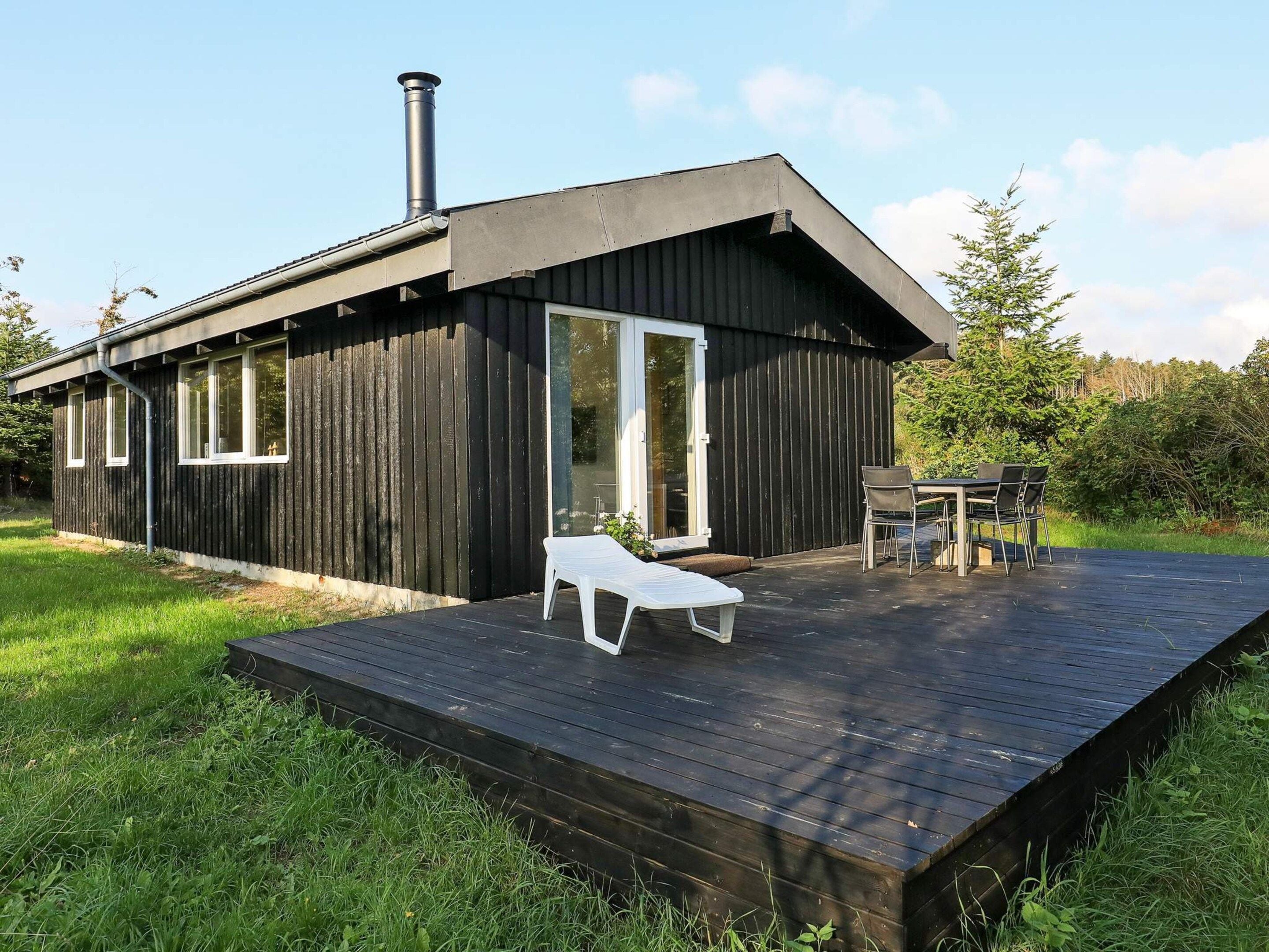 A modern cabin with a deck, a chimney, and a glass door.