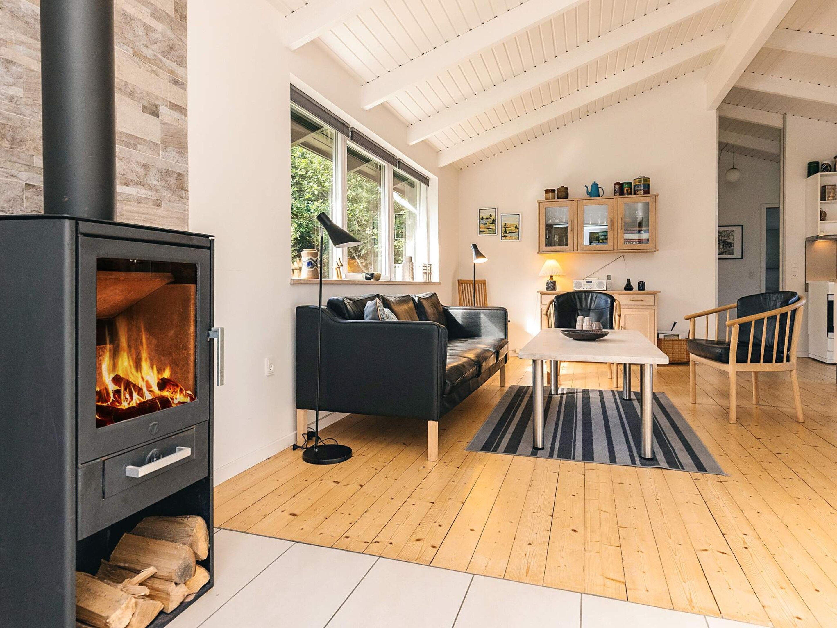 A modern living room with a wood-burning stove, a sofa, a dining table, and a kitchen area with cabinets and a refrigerator.