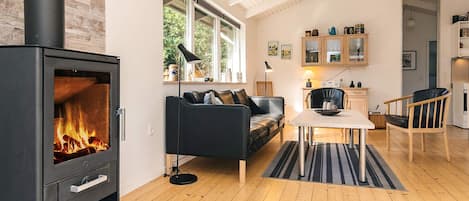 A modern living room with a wood-burning stove, a sofa, a dining table, and a kitchen area with cabinets and a refrigerator.
