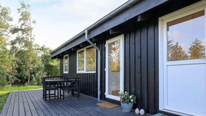 Une terrasse en bois avec une table et des chaises, un pot de fleurs et une porte avec une fenêtre.