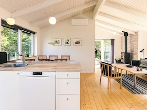 A modern kitchen with a built-in dishwasher, wooden dining table, and chairs, with a large window providing a view of the outdoors. - 4 Star Holiday Home in Lokken (Lokken)
