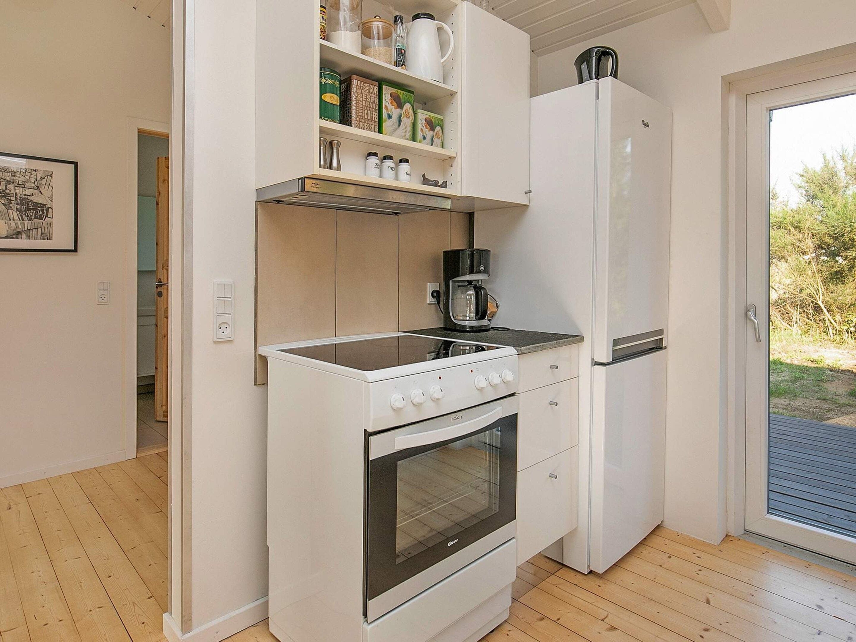 A compact kitchen with a white stove, oven, and refrigerator, a coffee maker on the countertop, and a door leading to a balcony.