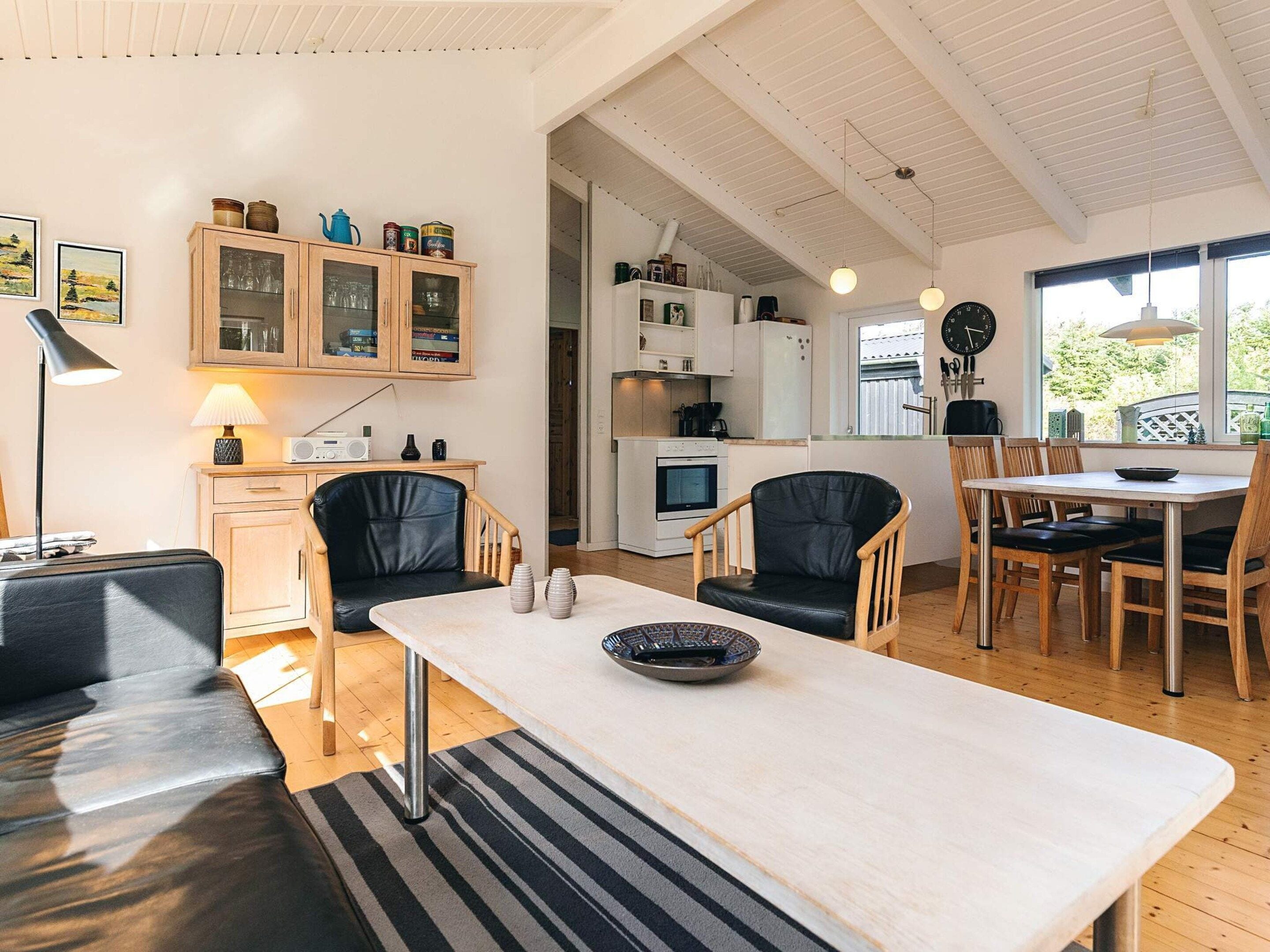 Une cuisine moderne avec des meubles blancs, un coin repas comprenant une table et des chaises, et un salon avec un canapé et une lampe.