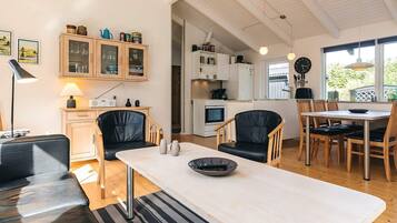 A modern kitchen with white cabinets, a dining area with a table and chairs, and a living room with a sofa and a lamp.