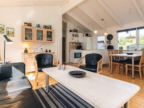 A modern kitchen with white cabinets, a dining area with a table and chairs, and a living room with a sofa and a lamp. - 4 Star Holiday Home in Lokken (Lokken)