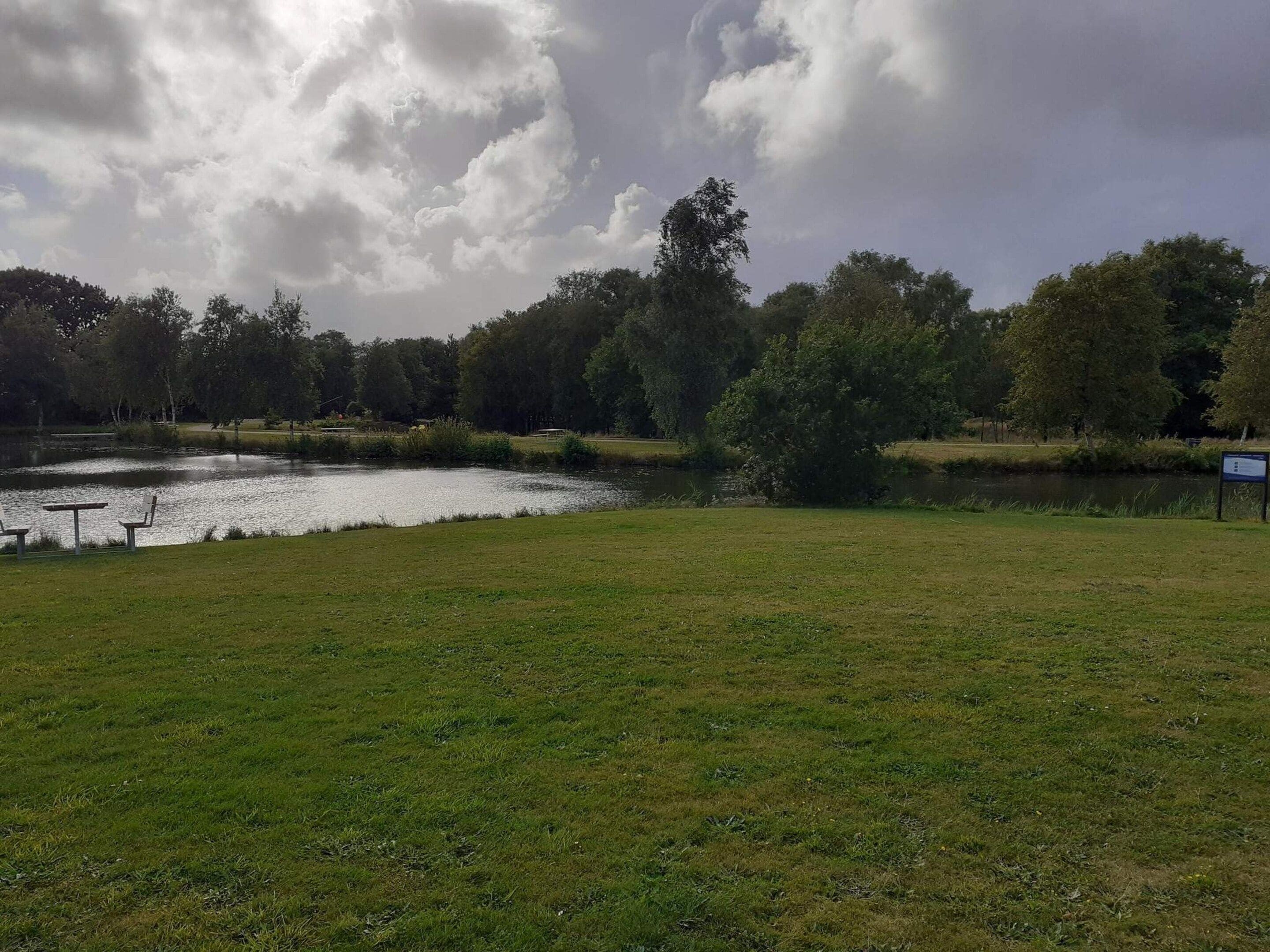 Un parque con un estanque, mesas de picnic y un cartel.
