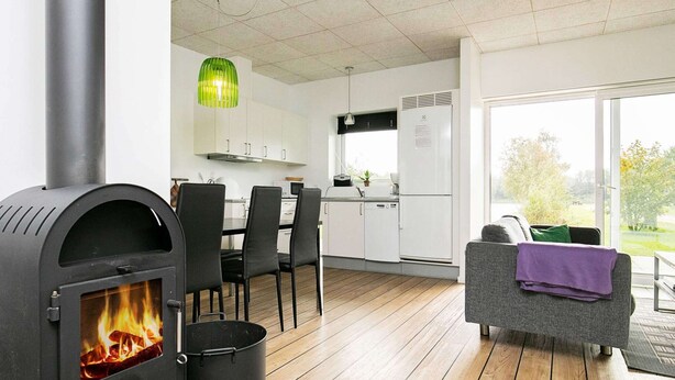A modern kitchen with a wood-burning stove, a dining area with chairs, and a sofa with a blanket. - 5 Star Holiday Home in Ringkobing (Ringkobing)