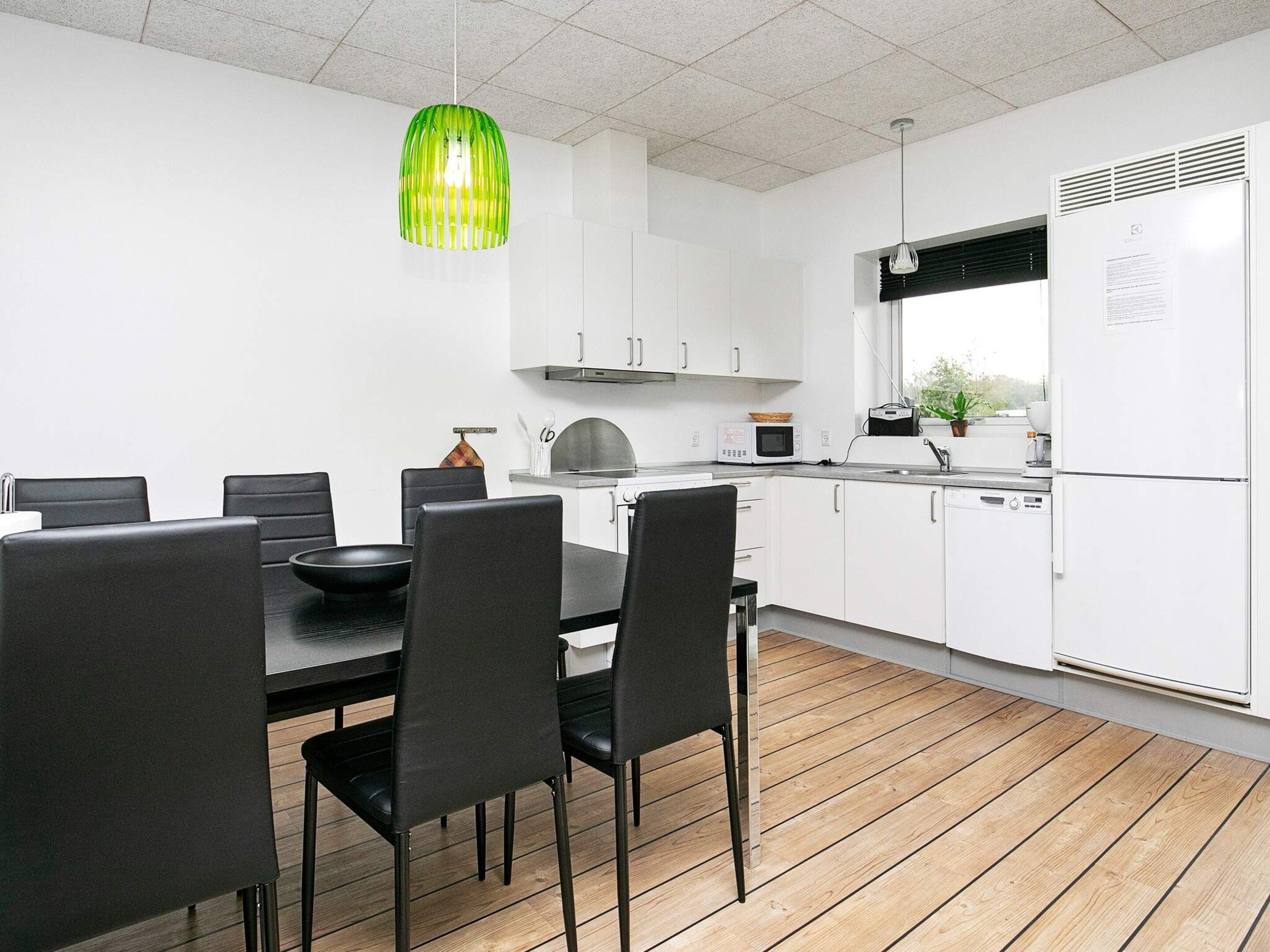 A modern kitchen with white cabinets, a dining table with chairs, a microwave, and a refrigerator.