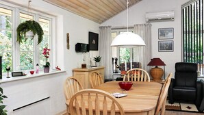 A dining area with a wooden table and chairs, a hanging light fixture, and a view of the outdoors through large windows. - 5 Star Holiday Home in Hadsund (Hadsund)