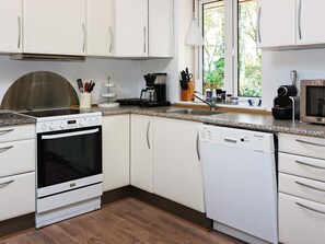 A modern kitchen with white cabinets, a stainless steel range hood, a built-in oven, a dishwasher, and a coffee maker.