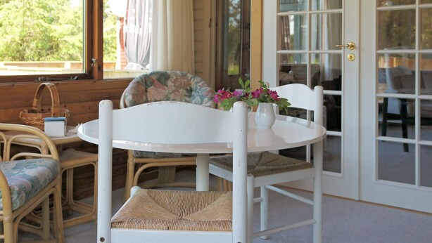 A white round table with two wicker chairs, a vase with flowers, and a wicker basket on the floor. - 6 Person Holiday Home in Lokken (Lokken)