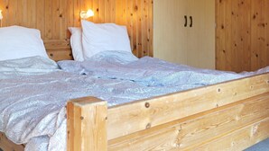 A wooden cabin-style room with a bed, two white pillows, a patterned blanket, and a wooden wardrobe. - 6 Person Holiday Home in Lokken (Lokken)