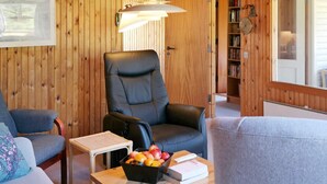 A cozy room with wooden walls, a leather chair, a small table with a fruit bowl, and a bookshelf. - 6 Person Holiday Home in Lokken (Lokken)