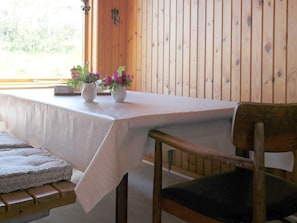 A wooden interior with a table covered by a white tablecloth, a bench with a cushion, and a chair with a dark cushion.