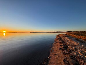 Un lac paisible au coucher du soleil, avec une plage de sable et une rive lointaine.