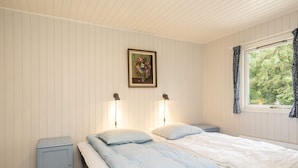 Une chambre à coucher avec un lit, deux tables de chevet, une commode, un tableau encadré au mur et une fenêtre avec des rideaux.