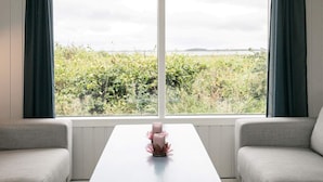Une pièce dotée d’une grande fenêtre, de deux canapés gris, d’une table blanche et d’un vase rose servant d’élément décoratif.