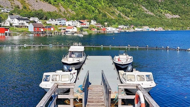 A dock with two boats, a wooden pier, and a backdrop of houses and hills.