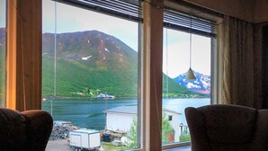 A room with a large window offering a view of a lake and mountains. There are two chairs in the foreground.