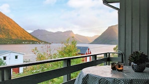 A balcony with a view of a lake, mountains, and a small house.