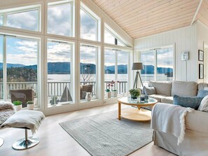 A spacious room with large windows offering a view of a lake and mountains. There is a round coffee table, a sofa, and a chair. - Holiday Home in ValevÃ¥g (Sveio)