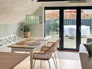 Et moderne interiør med spiseplads, fletstole, en potteplante og udsigt til en udendørs terrasse med et overdækket bord.