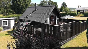 Ett trähus med ett sluttande tak, en inhägnad trädgård och en liten veranda.