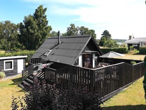 Een houten huis met schuin dak, een omheind erf en een klein terras.