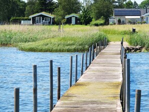Een houten steiger die zich uitstrekt over een wateroppervlak, omringd door grasvelden en kleine gebouwen.