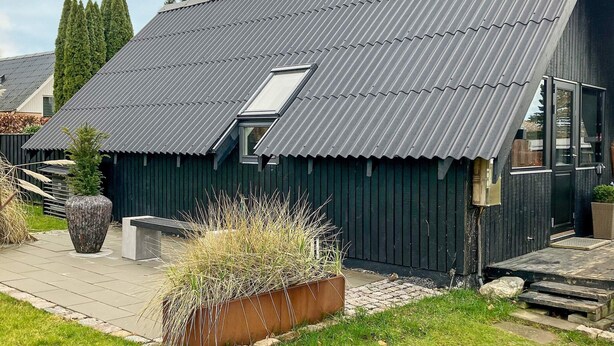 Ett modernt hus med ett sluttande tak av metall, ett takfönster och en träaltan.