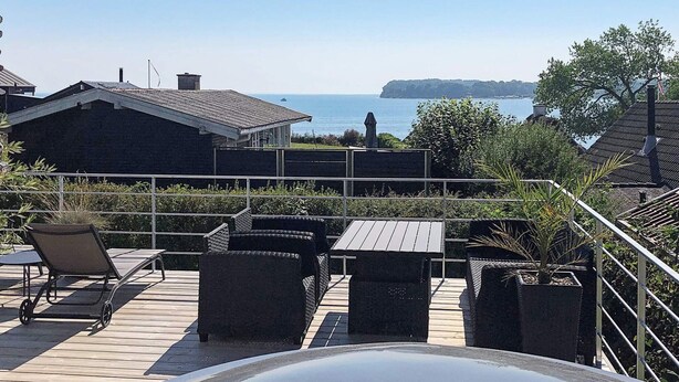A patio with outdoor furniture, a view of the sea, and a distant island. - 4 Star Holiday Home in Hejls (Hejls)