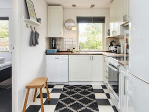 A compact kitchen with white cabinets, a built-in dishwasher, a coffee machine, and a window with a view of greenery. - 4 Star Holiday Home in Hejls (Hejls)